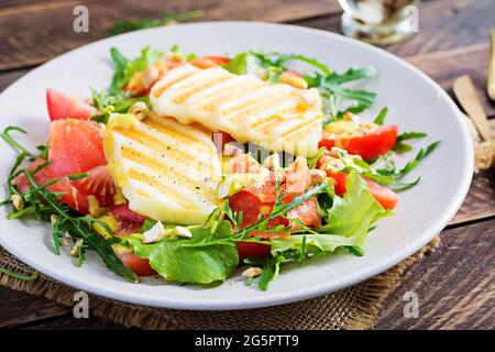 Gegrillter Halloumi-Käsesalat mit Salzlachs, Tomaten und grünen Kräutern. Gesundes Essen auf dem Teller auf Holzgrund. Stockfoto