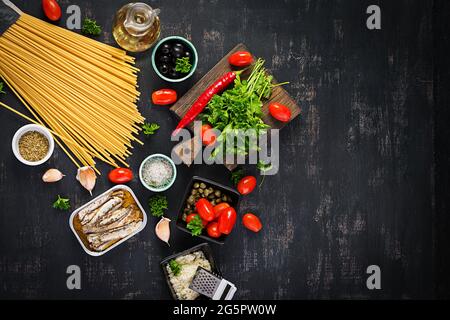 Zutaten zum Kochen von Pasta Spaghetti alla puttanesca - italienisches Nudelgericht mit Tomaten, schwarzen Oliven, Kapern, Sardellen und Petersilie. Draufsicht, FLA Stockfoto