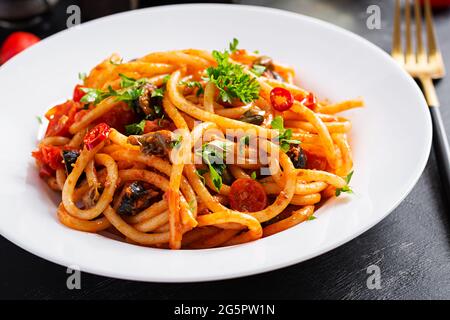 Spaghetti alla Puttanesca – italienisches Nudelgericht mit Tomaten, schwarzen Oliven, Kapern, Sardellen und Petersilie. Stockfoto