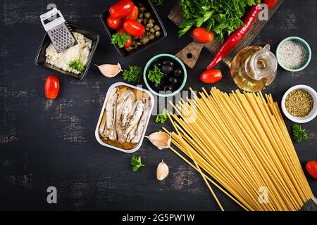 Zutaten zum Kochen von Pasta Spaghetti alla puttanesca - italienisches Nudelgericht mit Tomaten, schwarzen Oliven, Kapern, Sardellen und Petersilie. Draufsicht, FLA Stockfoto