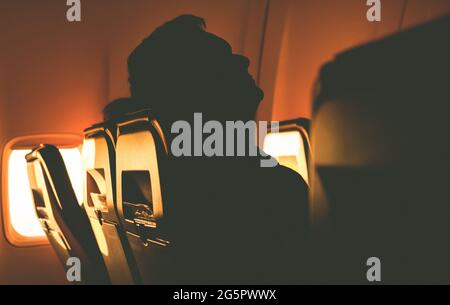 Schlafende touristische Silhouette im Flugzeugsessel bei Sonnenaufgang aus dem Bullauge Stockfoto