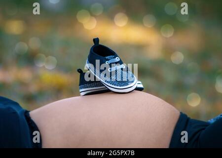 Fotos von einem Paar winziger Schuhe auf dem Bauch einer Schwangeren Stockfoto