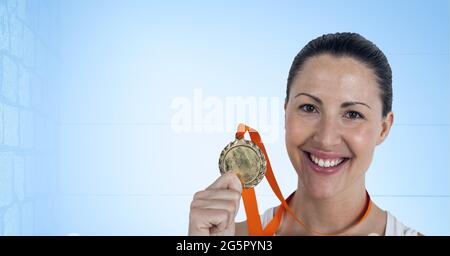 Porträt einer kaukasischen Athletin, die eine Medaille um den Hals hält und vor blauem Hintergrund lächelt Stockfoto