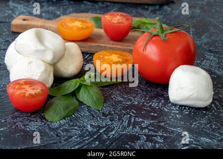 Mozzarella-Kugeln, Tomaten und Basilikum auf schwarzem Hintergrund. Zutaten aus italienischem Caprese-Salat. Weicher Fokus. Draufsicht Stockfoto