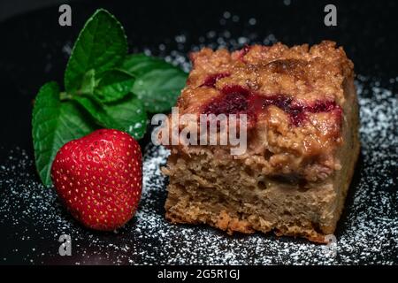 Nahaufnahme eines frisch gebackenen Kuchens mit Himbeeren, Jostabern und Rhabarber auf einem schwarzen Teller isoliert auf schwarzem Hintergrund mit Minzblättern und str Stockfoto