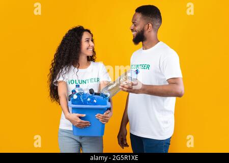 Zwei Verschiedene Freiwillige Setzen Plastikflasche In Box, Gelber Hintergrund Stockfoto