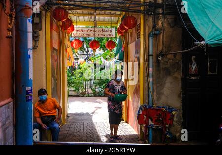 Die Menschen gehen in einer engen, sonnendurchfluteten Gasse in der Nähe von Klong Ong Ang in Bangkok, Thailand, ihren täglichen Geschäften nach Stockfoto