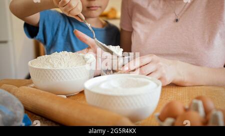 Nahaufnahme eines kleinen Sohnes, der Mutter hilft, Mehl in eine Schüssel zu gießen, um Kekse oder Teig zu machen. Kinder kochen mit Eltern, kleiner Koch, Familie hat Zeit Stockfoto