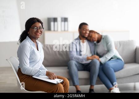 Fröhliche weibliche Psychologin und junges schwarzes Paar, das sich nach einer effektiven Therapie im Büro umarmt, Platz kopieren Stockfoto