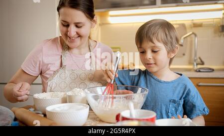 Kleiner netter Junge, der seiner Mutter dabei hilft, Teig für Kuchen oder Kuchen zu mischen. Kinder kochen mit den Eltern, kleiner Koch, Familie, die Zeit zusammen, häusliche Stockfoto