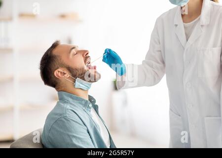 Arzt, der oralen Coronavirus-PCR-Test für jungen Mann in der Klinik macht. Millennial guy unterziehen covid diagnostischen Verfahren Stockfoto