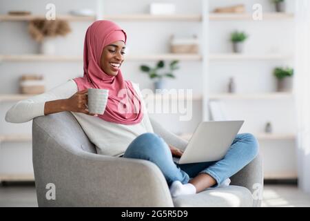 Schwarze Frau In Hijab Ruht Mit Laptop Und Kaffee Zu Hause Stockfoto