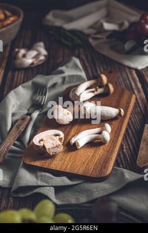Dunkle Fotografie von Pilzen, Spargel, Brot, Knoblauch und Pflaumen auf einem Tisch aus altem Holz. Gemüse Rezept für Herbst oder Winter. Moody Bild von Stockfoto