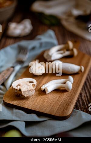 Dunkle Fotografie von Pilzen, Spargel, Brot, Knoblauch und Pflaumen auf einem Tisch aus altem Holz. Gemüse Rezept für Herbst oder Winter. Moody Bild von Stockfoto