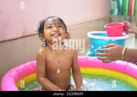 indischer Baby Junge genießt Bad in einem aufblasbaren Pool mit Wasser spritzt und schwimmt Spielzeug. Hochwertige Fotos Stockfoto