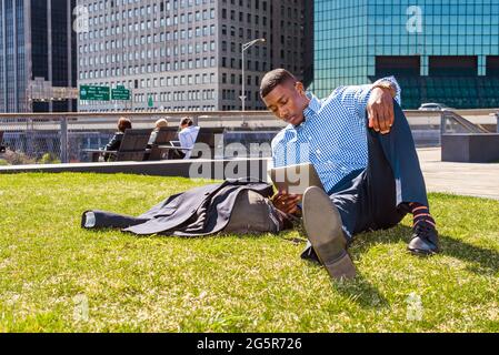 Studieren Im Freien. Ein junger schwarzer Mann sitzt auf einem grünen Rasen in New York City und liest auf einem Tablet-Computer. Stockfoto