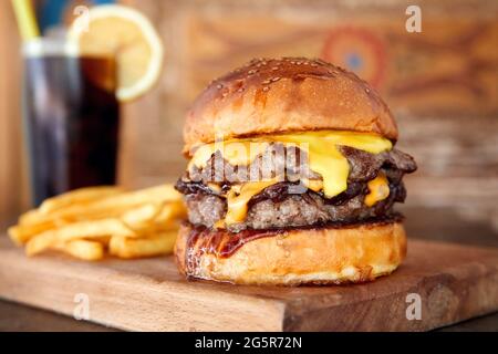 Köstliche hausgemachte Cheeseburger oder Hamburger auf Holztablett mit Cola und Feuer. Nahaufnahme von natürlichem Licht. Stockfoto