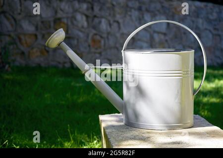 Metall-Gießkanne mit Garten, Gras und Wandhintergrund. Gartenkonzept. Stockfoto