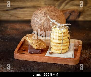 Hausgemachte Bio-Kokosnusskekse, Diätzuckerriegel und ganze Kokosnuss auf einem hölzernen Hintergrund. Glutenfrei, kohlenhydratarme Süßigkeiten mit Kokosnuss Stockfoto