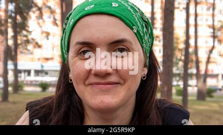 Nahaufnahme im Hochformat. Schöne junge Frau ohne Make-up in einem schwarzen T-Shirt und einem grünen Kopfschmuck von der Sonne an einem sonnigen Sommertag im Freien. Sonnenlicht Stockfoto