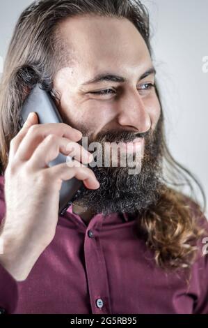 Porträt eines jungen Geschäftsmannes aus dem Nahen Osten mit Bart und langen Haaren, die lächeln, während er ein Gespräch auf dem Mobiltelefon führt Stockfoto