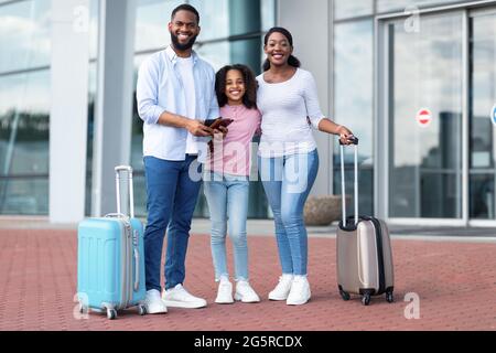 Glückliche schwarze Familie, die unterwegs war und Dokumente in der Nähe des Flughafens hielt Stockfoto