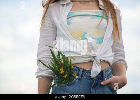 Nahaufnahme eines Blumenstraußes aus der Tasche der Denim-Hose eines Teenagers. Stockfoto