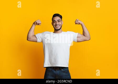 Lächelnder araber, der seinen Bizeps auf Gelb zeigt Stockfoto