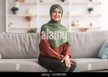 Glücklich Reif Muslimische Frau Trägt Hijab Sitzen Auf Sofa Im Innen Stockfoto