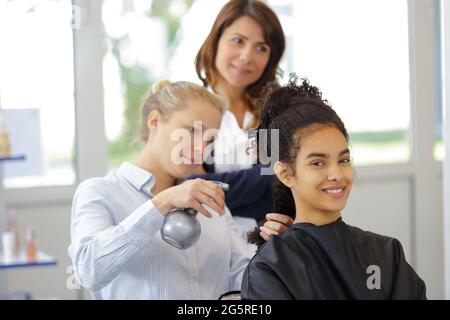 Friseurlehrling bügeln die Haare des Kunden Stockfoto