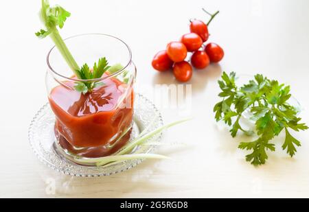 Tomatensaft in einem Glas, mit Petersilie und Sellerie-Sticks verziert. Stockfoto