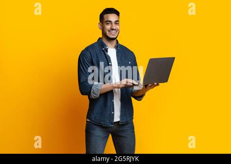 Hübscher arabischer Kerl, der seinen neuen modernen Laptop genießt Stockfoto