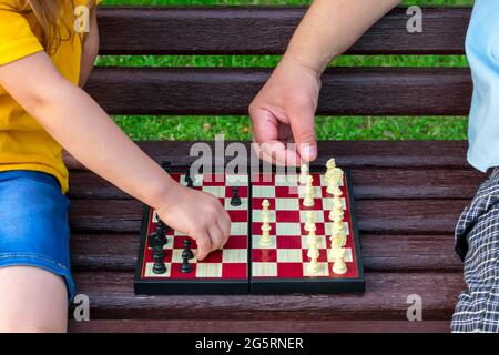 Kleines Mädchen spielt Schach mit Vater im Park auf einer Bank an der frischen Luft. Schachtag. Entwicklung, pädagogische Spiele. Stockfoto