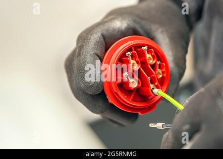 Hochspannungsstecker. Ein Elektriker, der Schutzhandschuhe trägt, schließt den 380-V-Hochspannungsstecker an. Panoramafoto Stockfoto