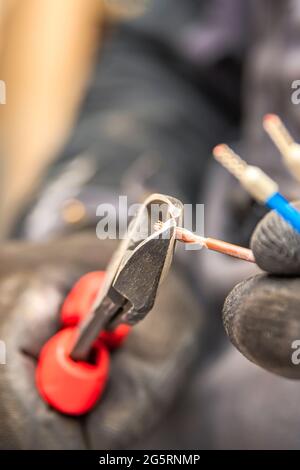 Elektriker schneidet elektrische Drähte mit Zangen, Installation von Haushaltsgeräten, Elektroinstallationsgeräte. Vertikales Foto Stockfoto