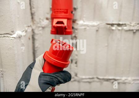 Stromkosten, Strompreis, Hochspannungs-Industriesteckdose. Hochspannungsstecker in der Hand. Anschließen eines dreiphasigen 380-Volt-Hochspannungssteckers Stockfoto