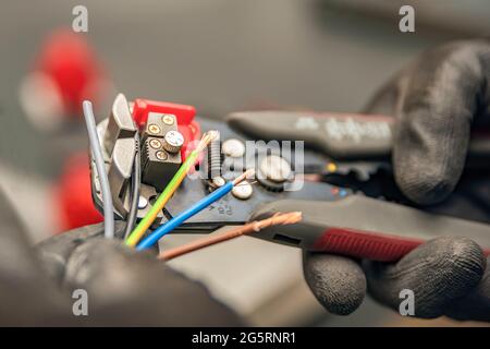 Abisolierzangen. Der Elektriker reinigt die Schutzisolierung vom Draht mit einem Abisolierer. Der Prozess der Verbindung von Drähten. Nahaufnahme Stockfoto