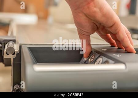 Die Hand drückt die Taste beim Einschalten einer Industriemaschine. Sägeblatt wird geschnitten. Schalter zur Steuerung von Industriemaschinen und Anlagen in Stockfoto