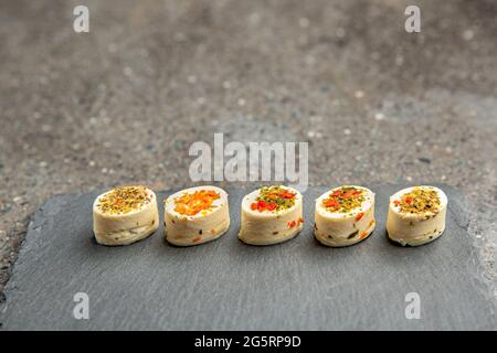 Käseplatte mit Gewürzen. Mazzarella Käse mit verschiedenen Gewürzen. Käsesnacks verschiedener Geschmacksrichtungen auf einem Tablett mit schwarzem Stein im Hintergrund oder auf einem Banner Stockfoto