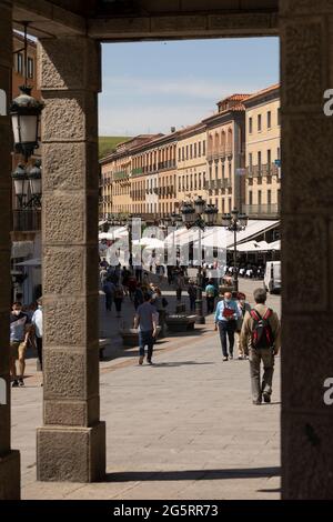 Segovia, Spanien - 2. Juni 2021: Mehrere Touristen laufen mittags entlang der Aqueduct Avenue, umgeben von traditionellen Häusern, Bars und Restaurants Stockfoto