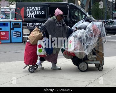 Obdachlose alte Frau, die ihre Belongiongs in der Flatbush Avenue vor der Long Island Railwqy Station und der Atlantic Mall in Brooklyn, New York, in die Länge schiebt. Stockfoto