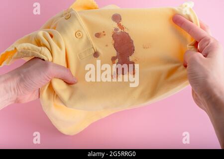 Weibliche Hände zeigen Blutflecken auf einer gelben Kleidung. Isoliert auf rosa Hintergrund. Hochwertige Fotos Stockfoto