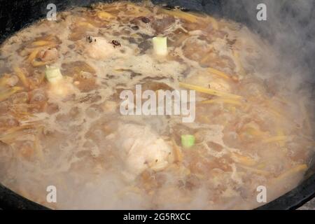 Zirvak für Pilaf, Fleisch, Lammfett, gelbe Karotten, Kichererbsen, Knoblauch und Gewürze werden in einem großen schwarzen Kessel mit Blasen und Dampf gebraten und garen foo Stockfoto