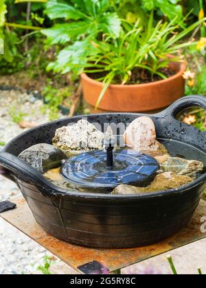 Kleiner Solarbrunnen in einem improvisierten Gartenvogelbad mit Kopfsteinpflaster zum Trinken und Baden Stockfoto