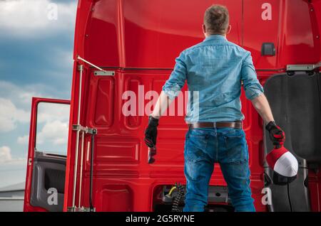 Überraschte den kaukasischen Semi Trucker in den 30er Jahren, der auf dem fünften Rad seines LKWs blieb und auf Kabinenelemente schaute. Thema Transport. Stockfoto