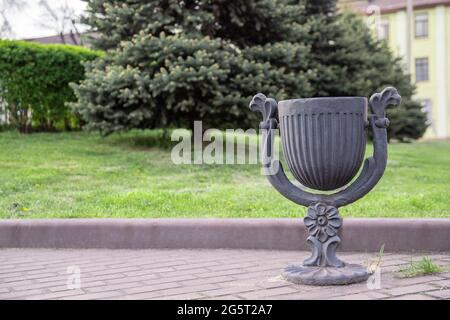 Metallisch grauer Müllcontainer am Fußweg im Stadtpark. Der Mülleimer steht im Park in der Nähe des Rasens vor dem Hintergrund der Natur. Stockfoto