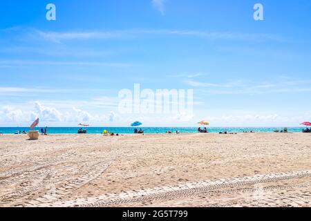 Hollywood, USA - 6. Mai 2018: Blick auf die Küste von Miami Florida während des Tages mit Menschen auf Sand sitzen auf Stühlen unter bunten Sonnenschirm mit Wasser ho Stockfoto