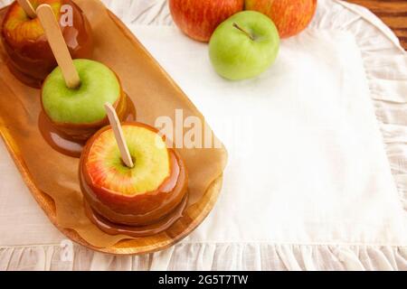 Eine Reihe von drei handgedippten hausgemachten Karamelläpfeln auf einer weißen Tischdecke Stockfoto