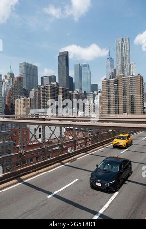 Ein Taxi und ein Auto über die Brooklyn Bridge von oben gesehen. Im Hintergrund ist die Skyline von New York zu sehen. Stockfoto