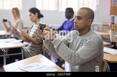 Hispanic Mann mit Smartphone während der Vorlesung in der Schule für Erwachsene Stockfoto